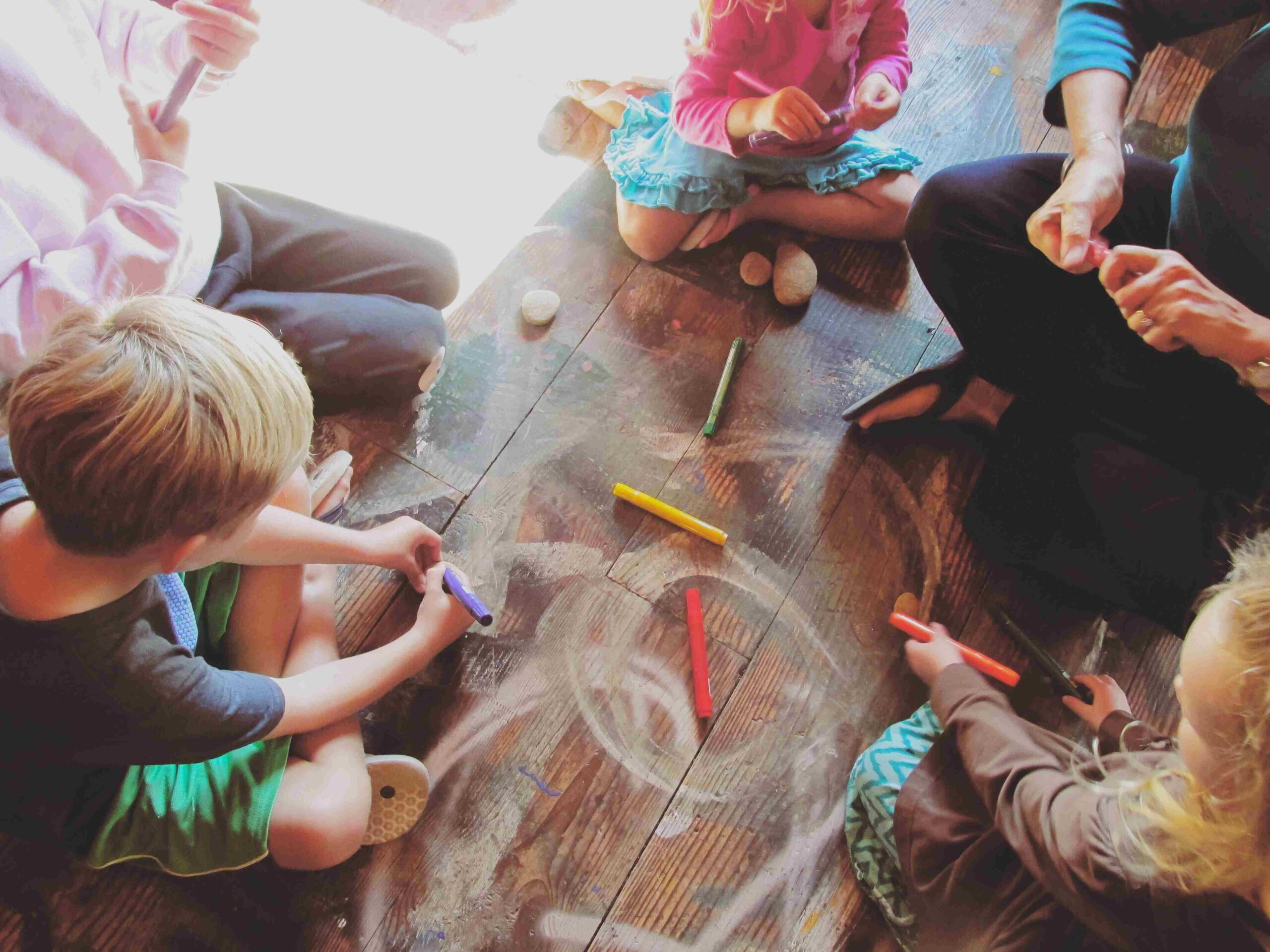 Children sitting in a circle drawing with markers on a wooden floor