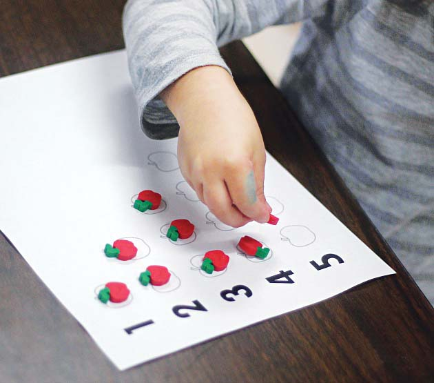 Child counting numbers 1–5 with red play-dough apples